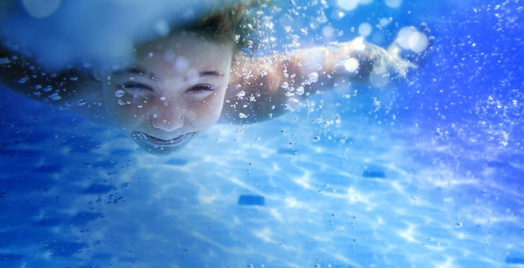 Wasseroberfläche mit spritzenden Wassertropfen und einem teilweise sichtbaren Arm unter Wasser